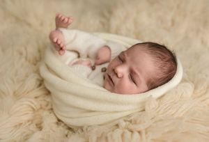 Baby boy wrapped in cream knits sleeps against a neutral lambswool rug, captured by Charlottesville maternity and newborn photographer.
