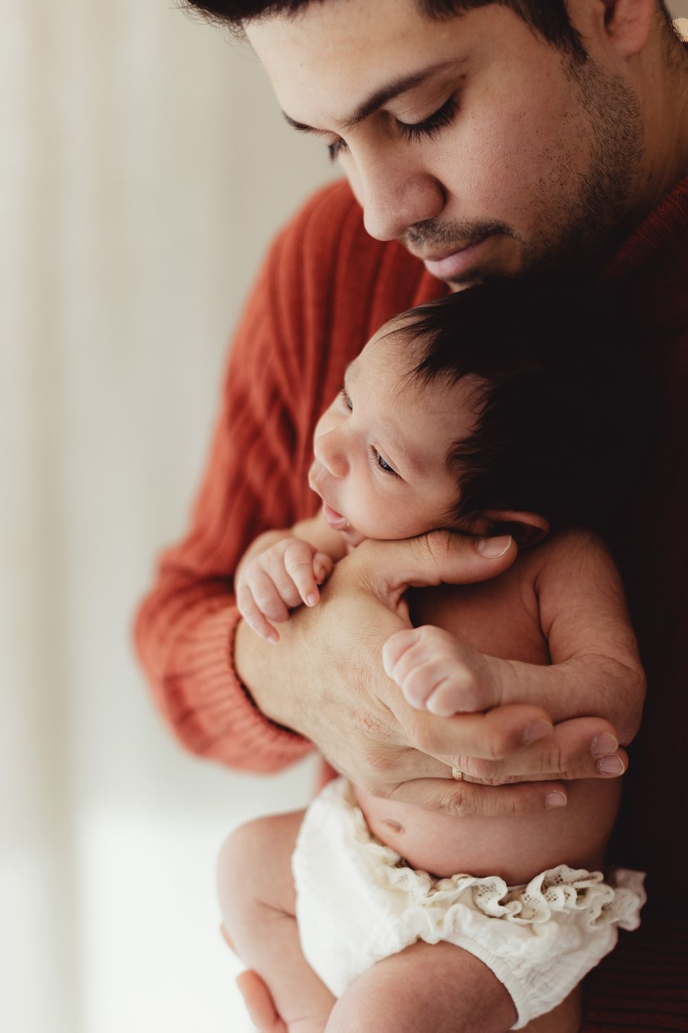 A tender moment captured in a series of photos showing a parent in a rust-colored sweater embracing and kissing a newborn baby.
