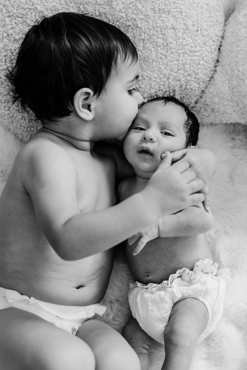 A tender black and white portrait of two young siblings in diapers sharing an intimate moment together.