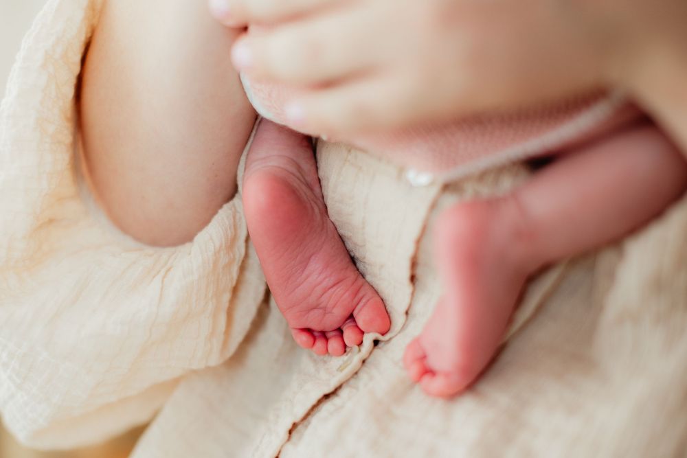 Close-up of a newborn baby's tiny feet wrapped in a soft cream blanket, held gently by a parent.