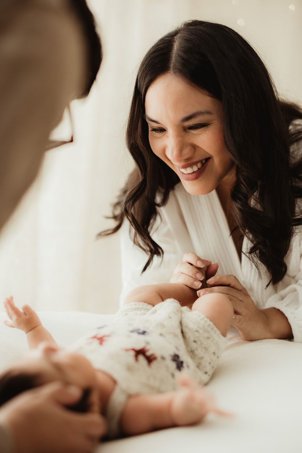 A joyful moment captured between mother and baby sharing laughter while lying on white bedding.