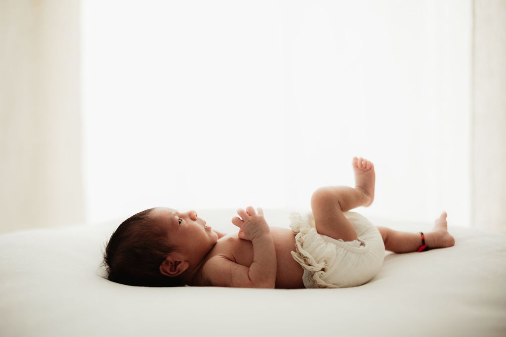 Newborn baby lying on white surface in diaper, looking up peacefully in bright natural light.
