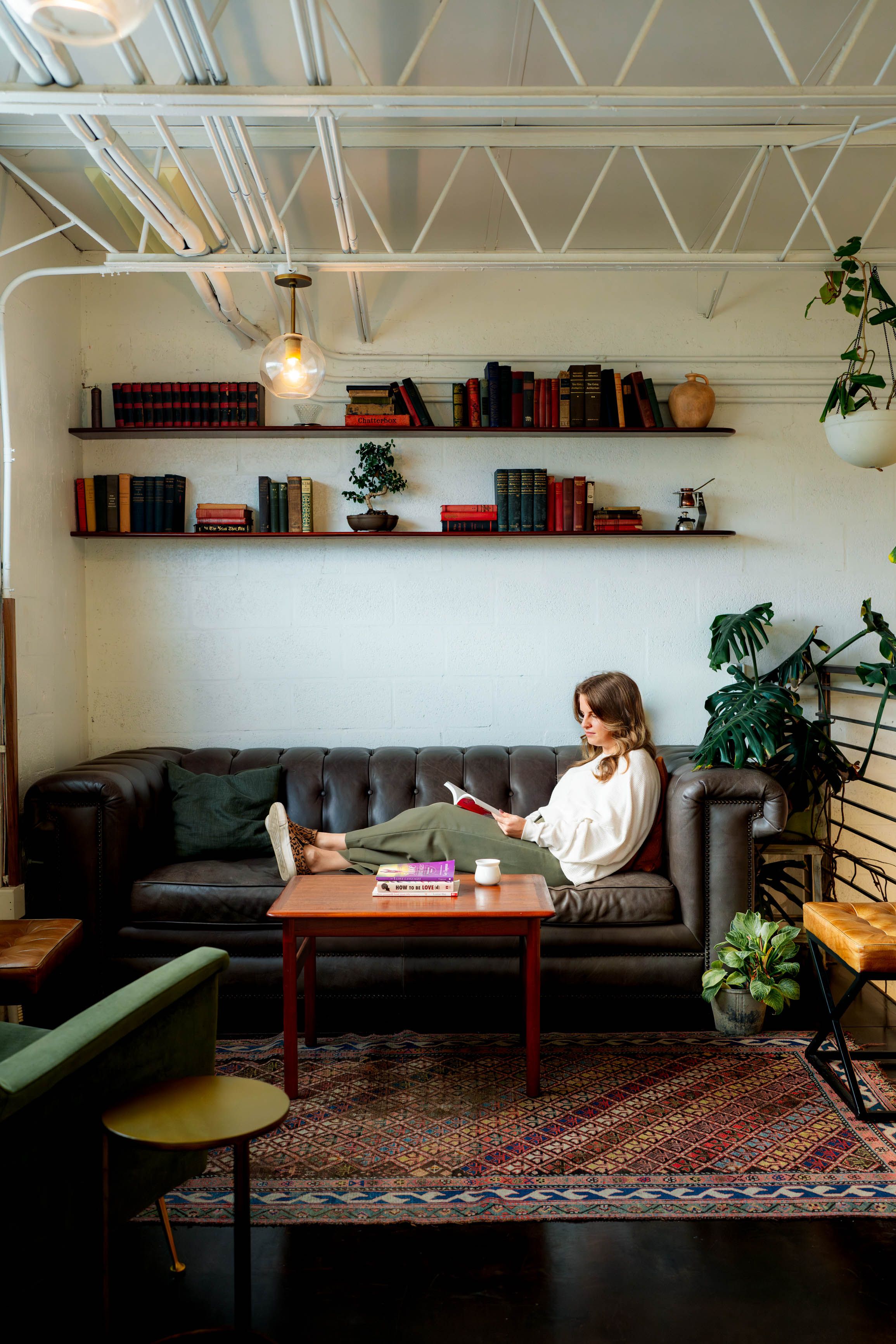 A minimalist living room with bookshelves, plants, and a person reading on a leather couch.