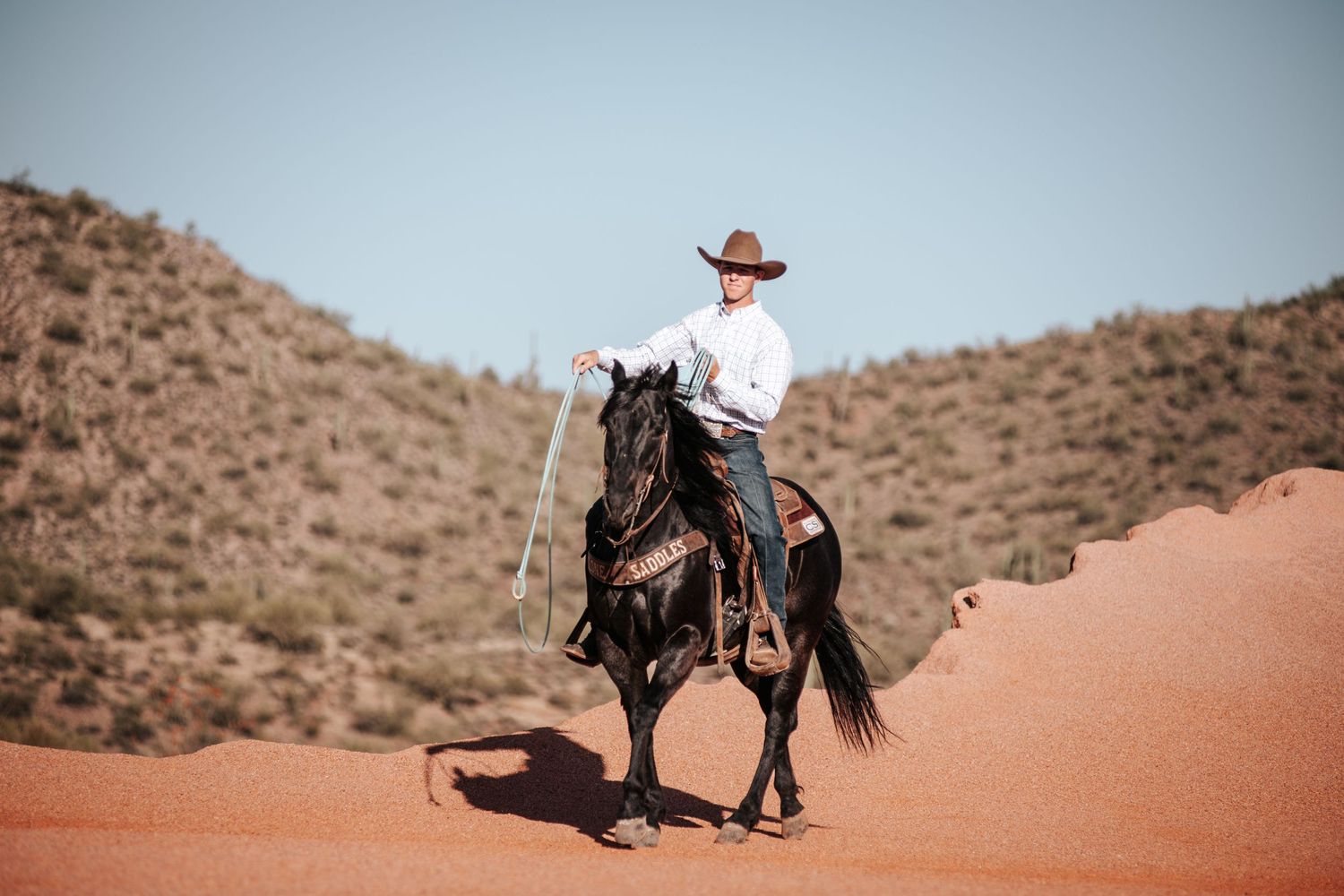 Desert horseback riding scene with rugged mountain terrain in the background.
