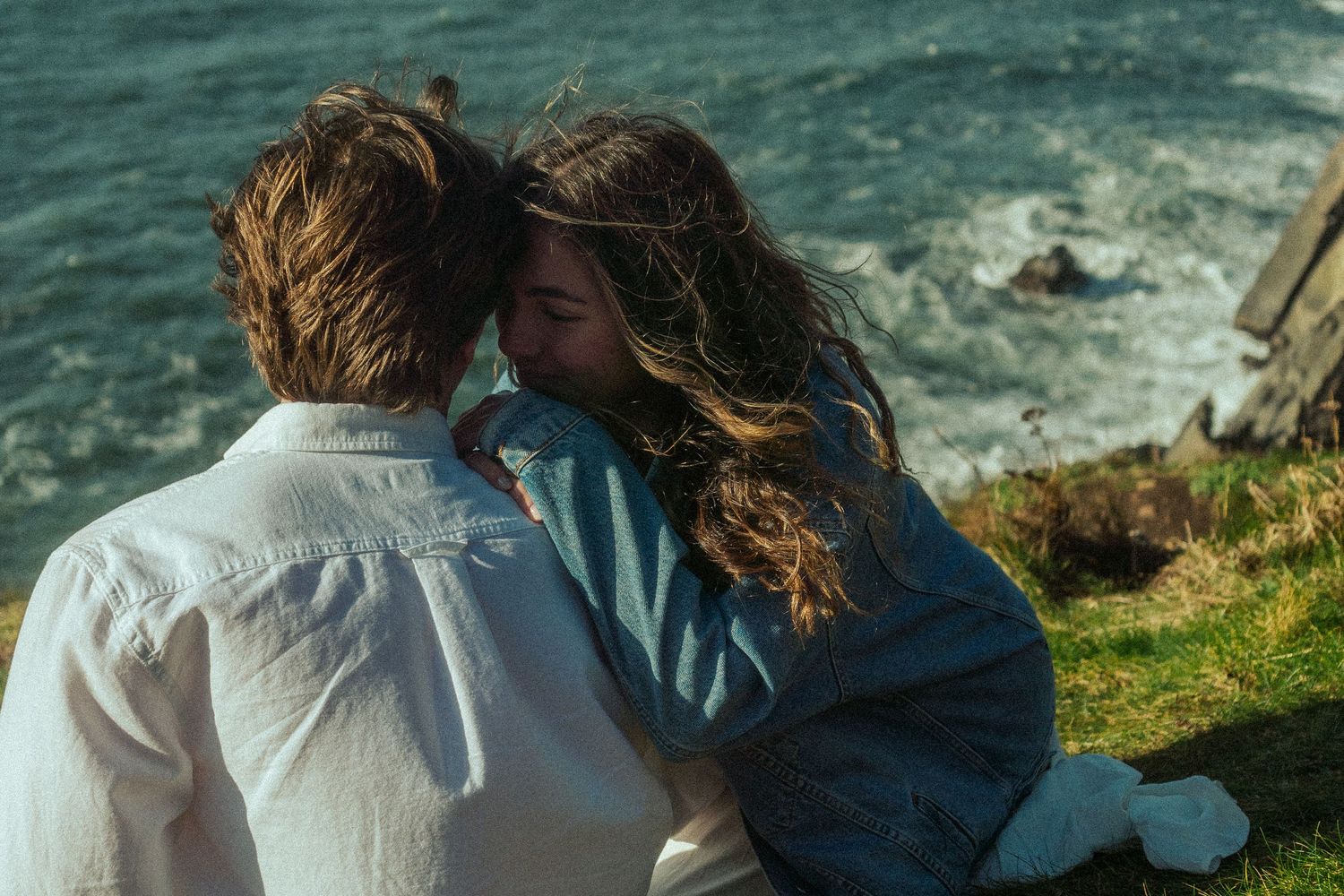 A couple sharing an intimate moment overlooking dramatic coastal cliffs and ocean waves.