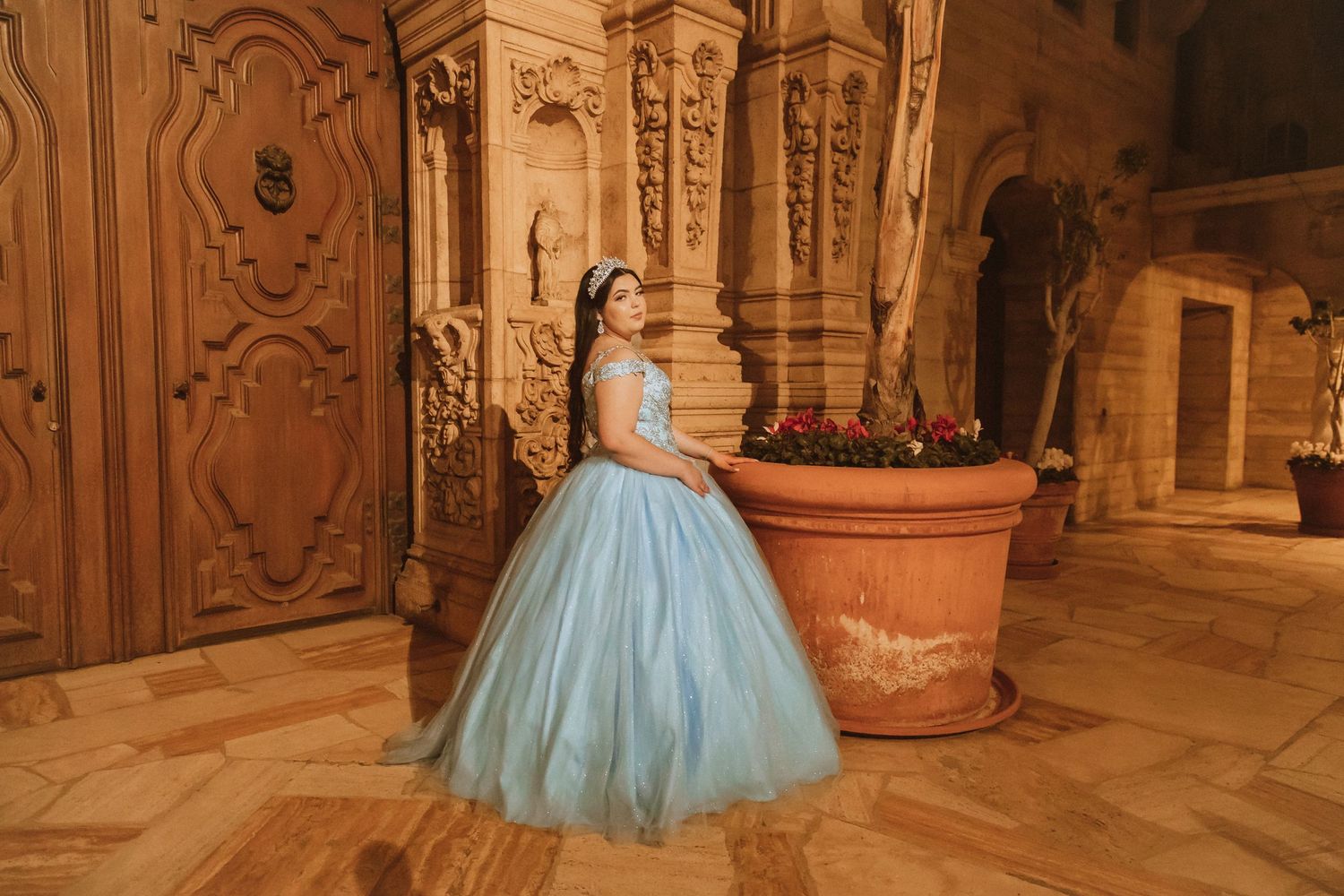 A light blue ball gown glows in an ornate stone interior with classical architecture.