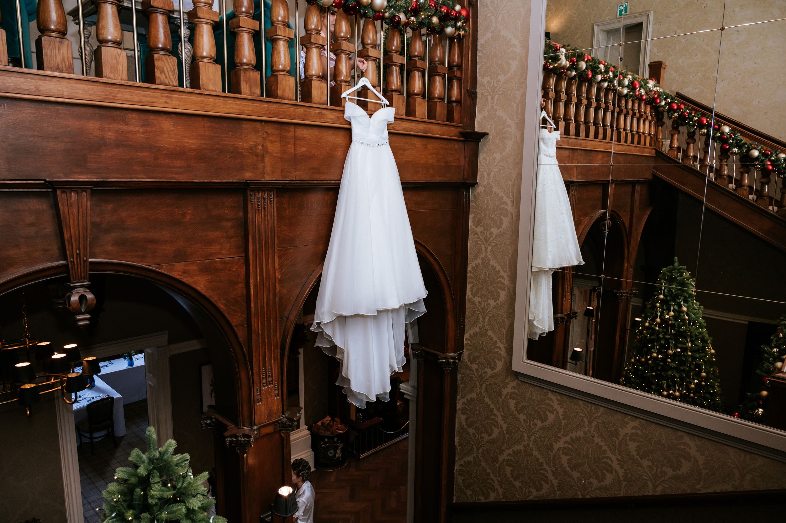 A row of elegant wedding dresses displayed on hangers against a wooden staircase backdrop in a bridal boutique.