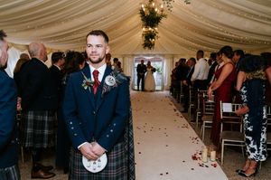 Wedding guests dance and celebrate on a decorated dance floor under an elegant white tent with hanging lights.
