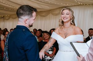A couple exchanges vows during their wedding ceremony under twinkling lights and white fabric draping.