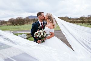 A romantic wedding moment captured outdoors with a flowing white veil and bouquet against a scenic countryside backdrop.