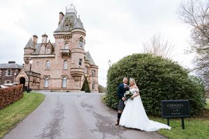 A wedding couple poses in front of a historic stone building with elegant architecture and landscaping.
