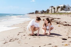Children playing and exploring together on sandy beach near ocean waves.