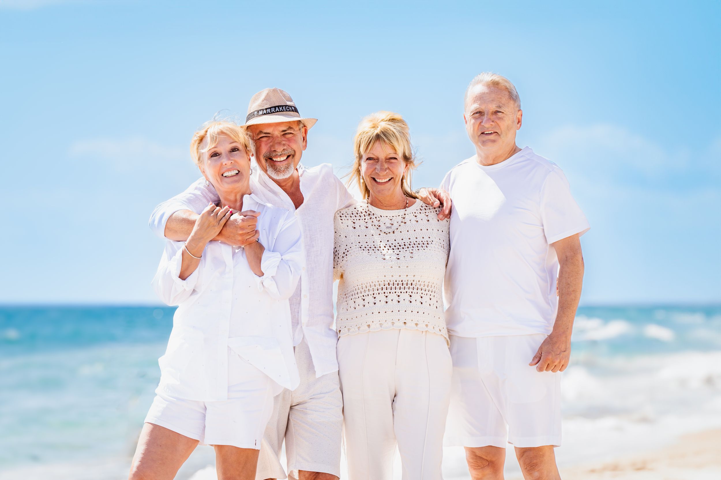 Group photo of people wearing white outfits on sunny beach with ocean waves behind them.