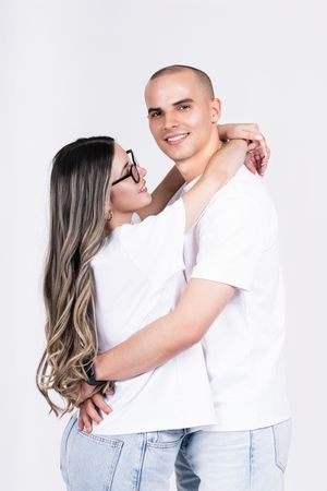 Couple in white shirts and jeans posing against white background.