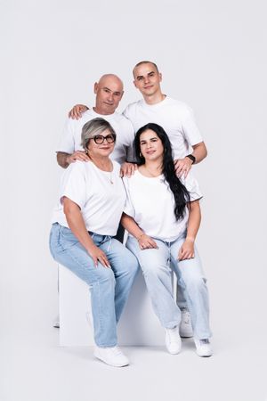 Group wearing matching white shirts and jeans pose together on white background.