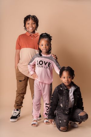 Children in casual outfits posing together against neutral beige background.