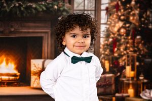 Young children in formal white outfits posing by Christmas decorations.