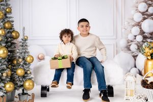 Children sitting together on white floor with Christmas decorations and gold ornaments.