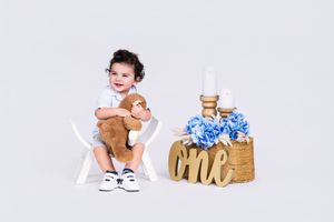 Baby in white outfit lies on floor with stuffed animals and decorative wooden blocks.