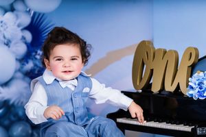 Baby photo session with blue balloon arch and gold 'one' text decoration.