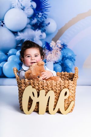 One year old birthday photos with wicker basket and blue balloon backdrop.