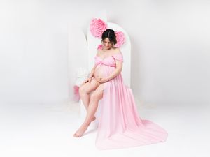 Maternity portraits featuring woman in flowing pink dress against white backdrop.