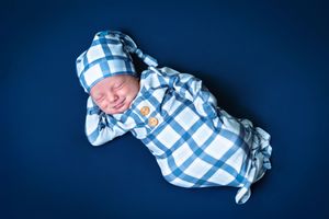 Baby wrapped in blue and white checkered blanket on dark blue background.