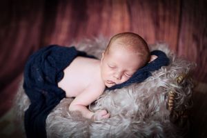 Sleeping baby on textured dark fur blanket in dim lighting.
