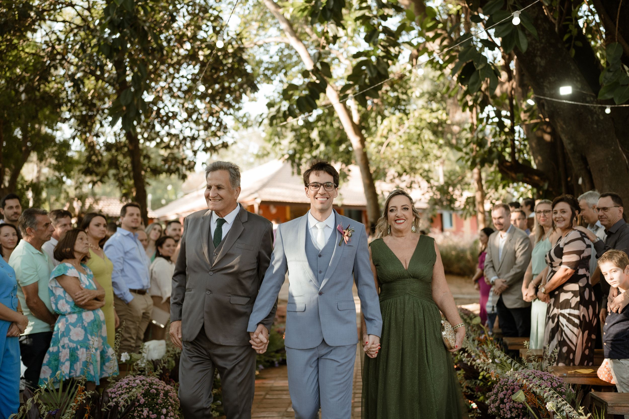 Outdoor wedding ceremony with guests seated under shady trees.