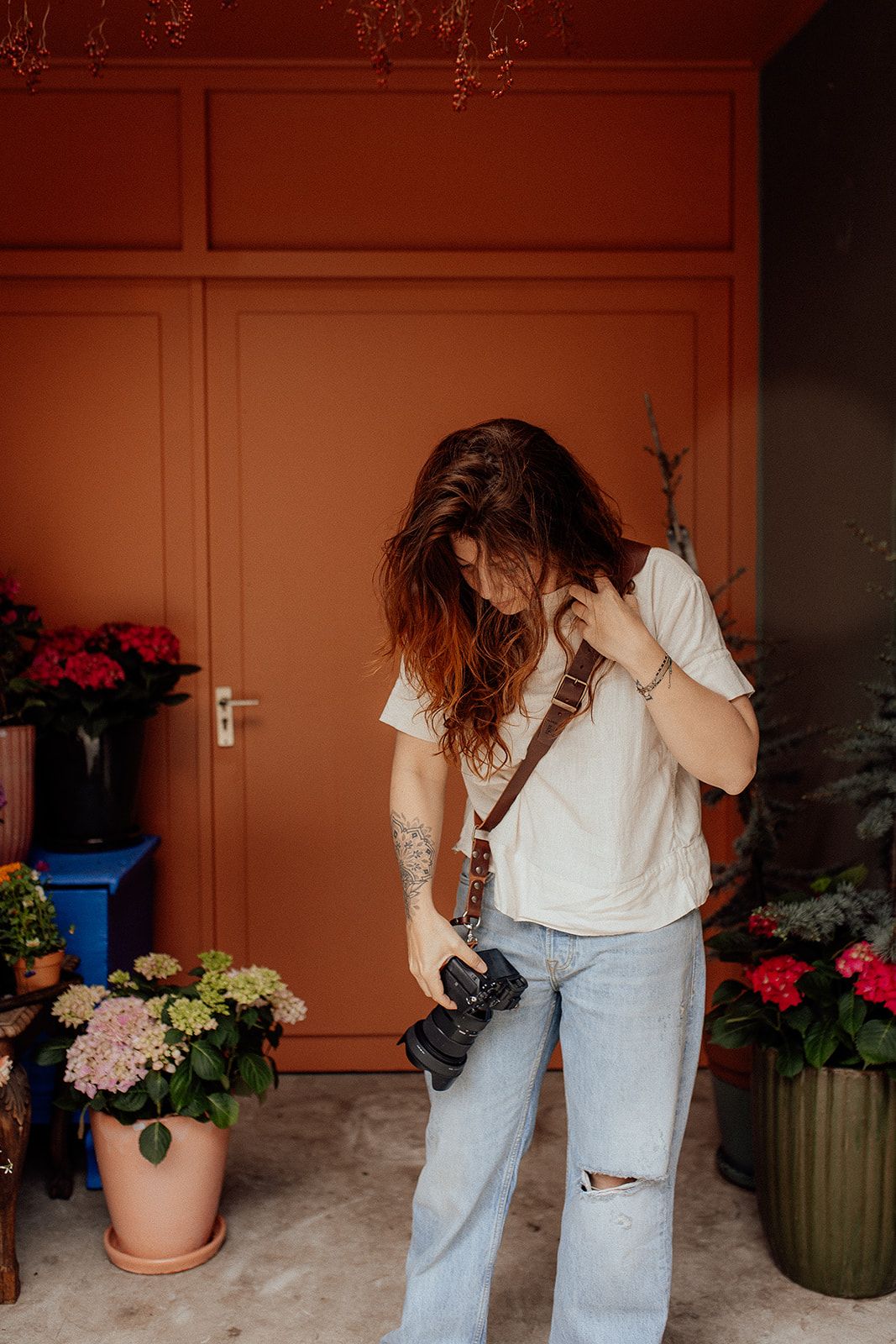 Photographer taking close-up photos of potted plants and flowers against terracotta colored wall.