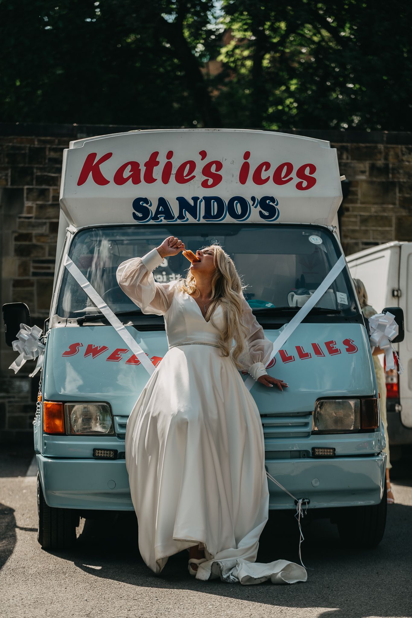 Vintage ice cream truck branded 'Katie's ices SANDO'S' with someone in a white dress drinking from a bottle.