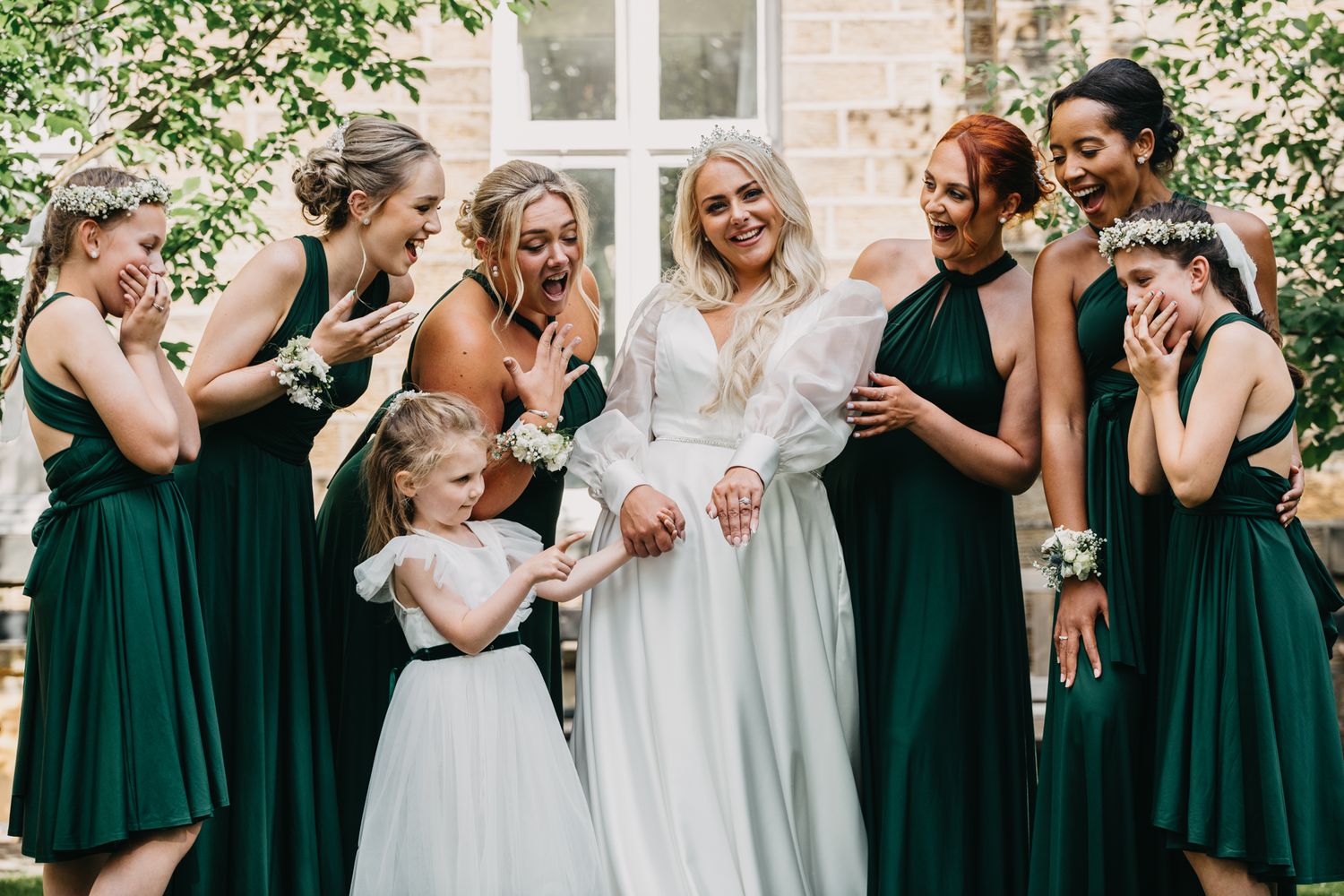 Wedding party in emerald green dresses sharing joyful moment together outdoors.