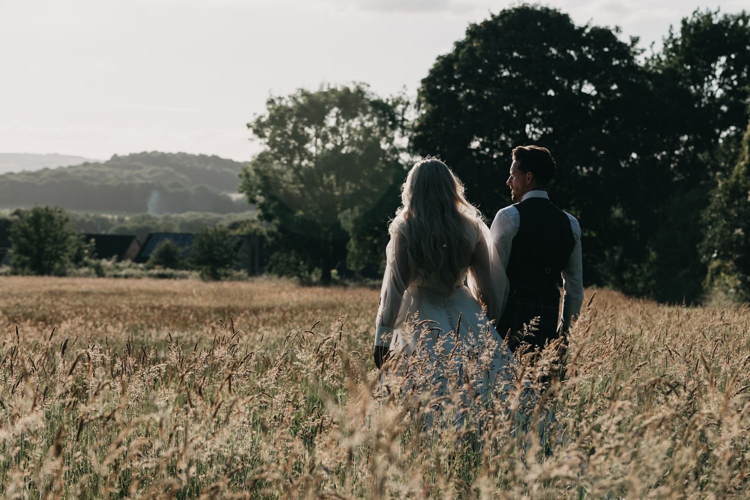 Couple walking together through a golden wheat field at sunset.
