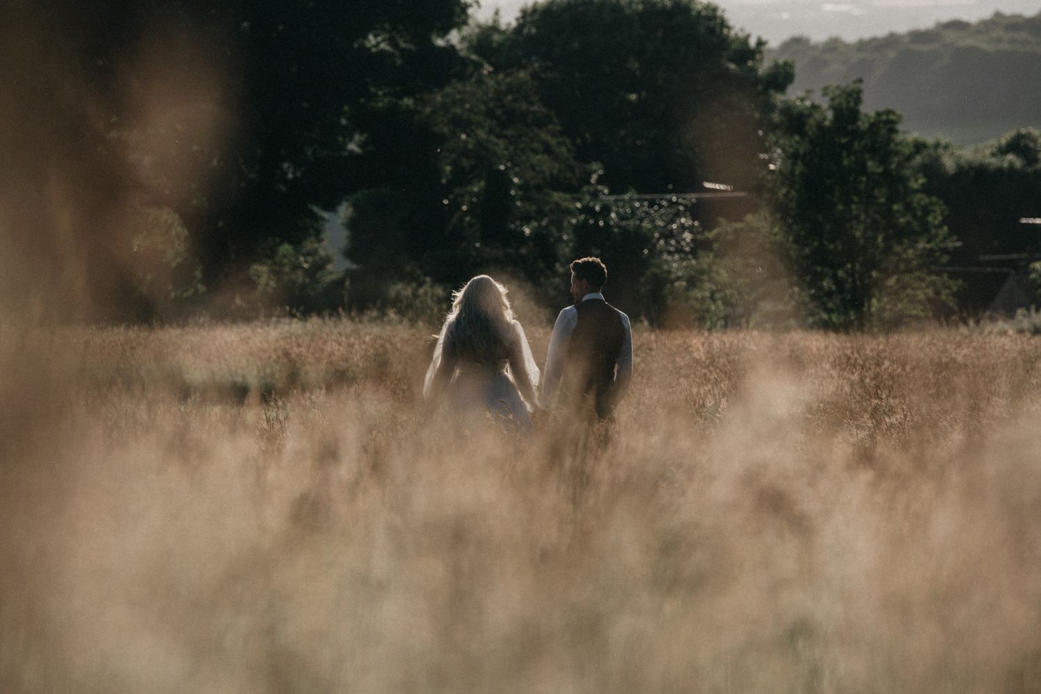 Silhouetted couple walking through misty golden field at sunset.