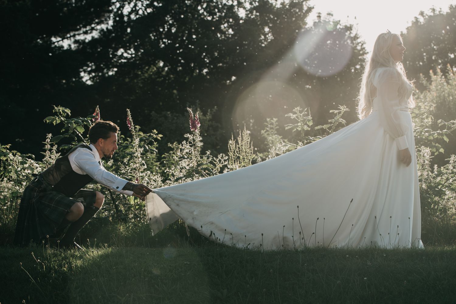 Sunlit wedding photo session with dress train spread in grass.