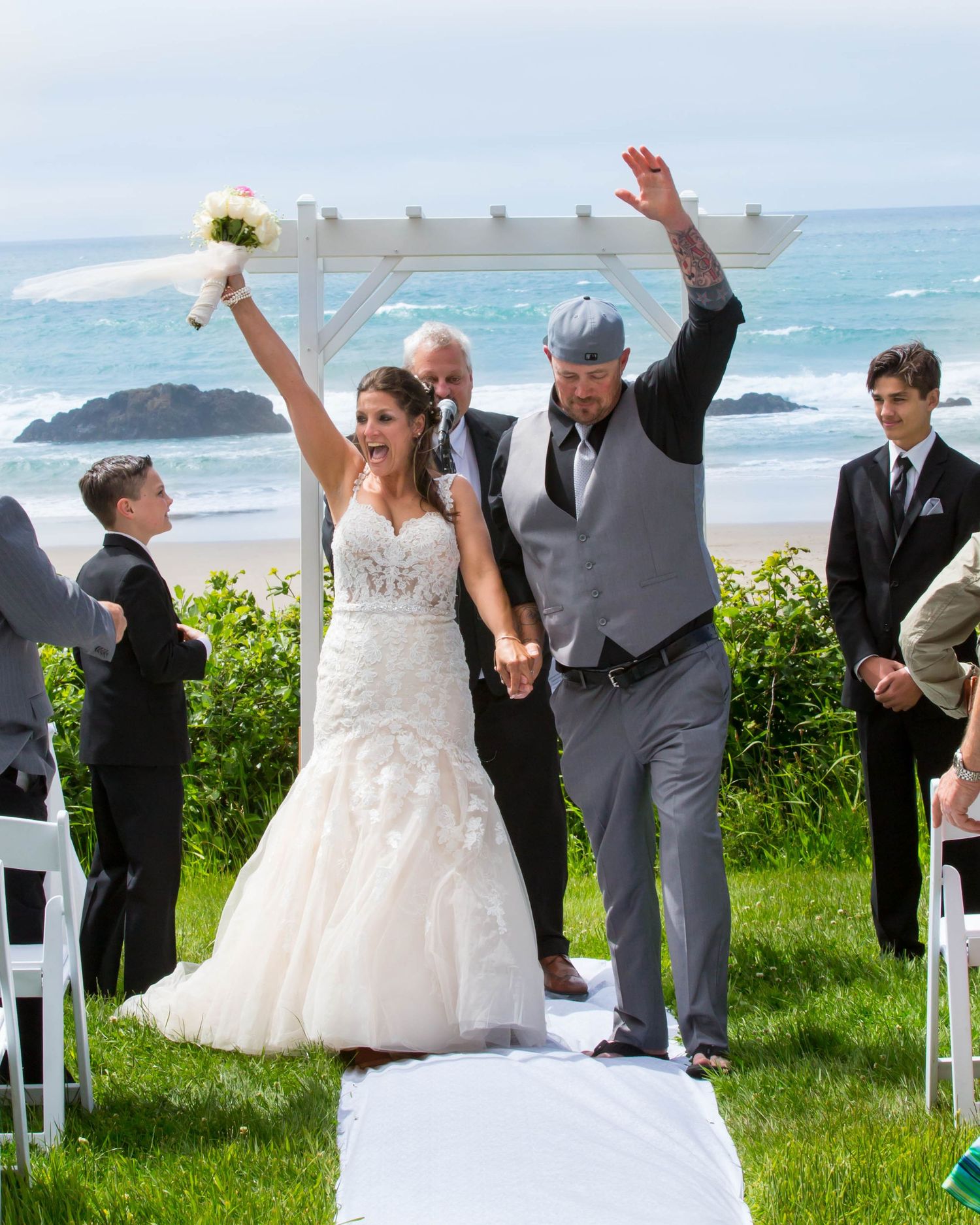 Wedding celebration on coastal cliff with couple and guests on white runner.