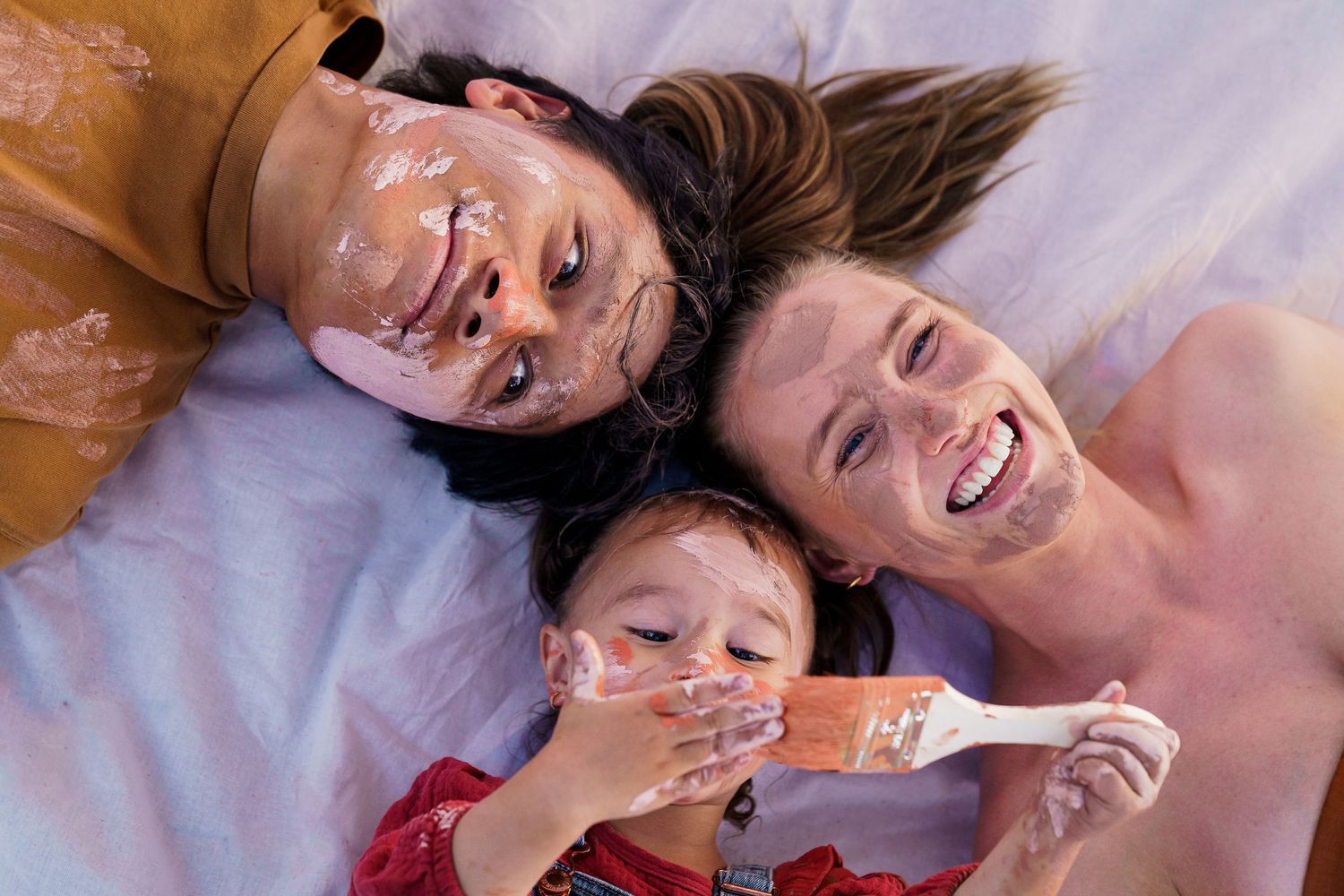 A family of three laying down on the ground for a family paint photo shoot session at The Dairy Western Sydney Parklands.