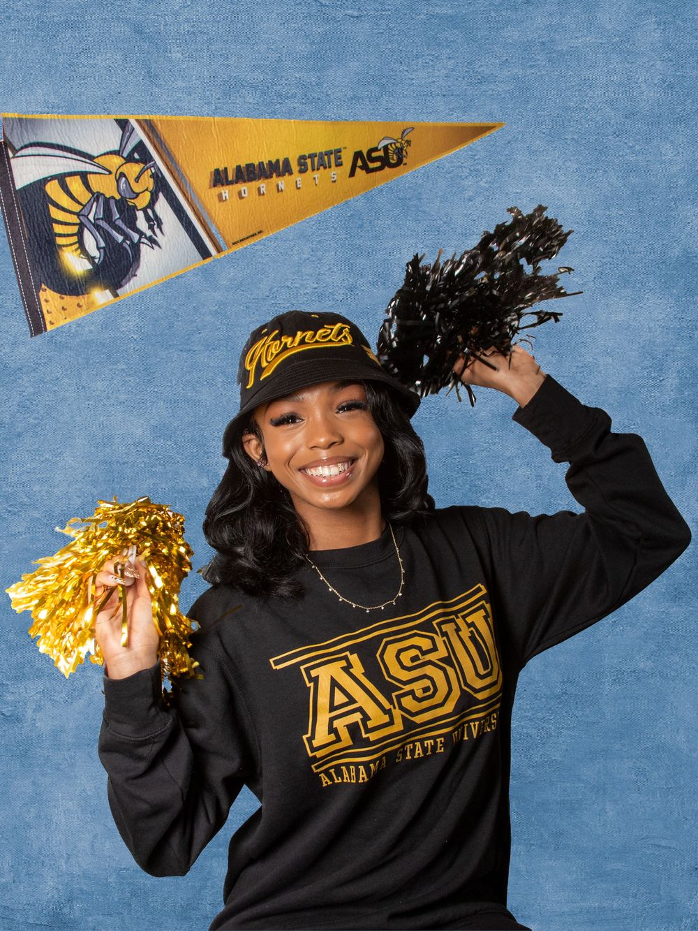 Student posing with Alabama State University ASU Hornets sweatshirt, cap, pom-poms, and pennant flag.