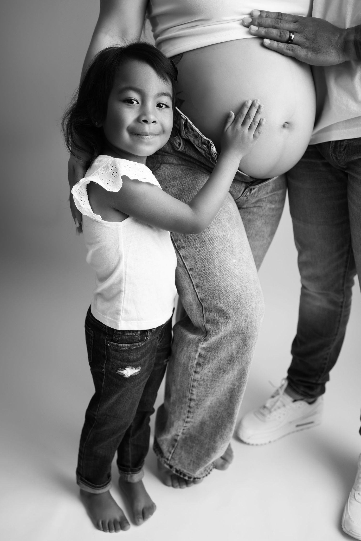 Young child hugging pregnant belly in black and white portrait.