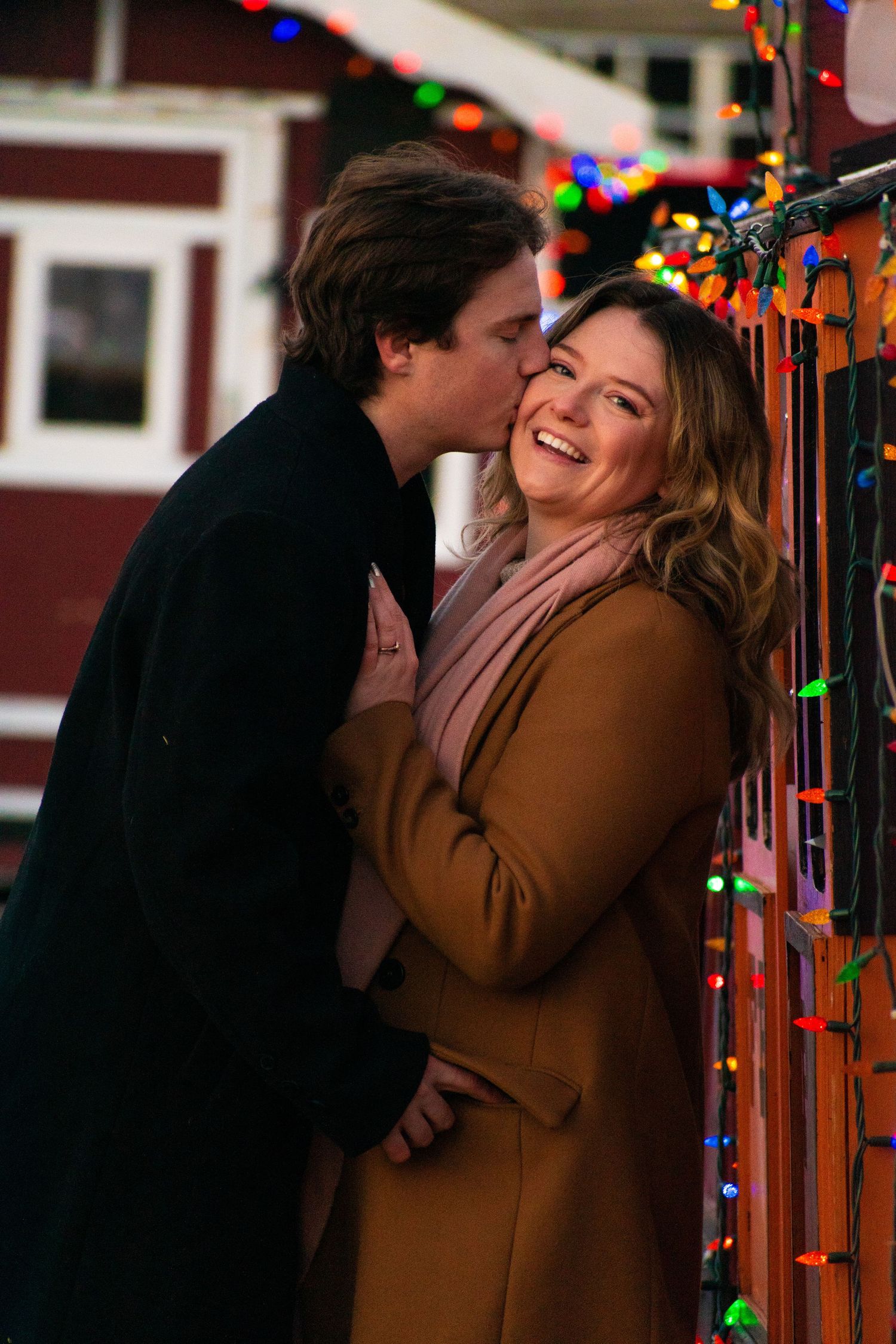 A sweet moment shared between a couple surrounded by colorful Christmas lights.