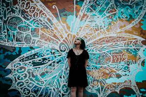 Person in black dress standing against wall with decorative butterfly wing street art mural.
