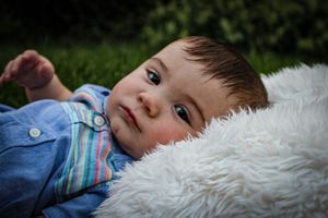 Close-up of baby in denim outfit lying on white furry blanket.