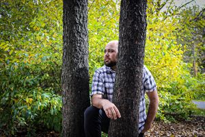 Person sitting between two tree trunks in a wooded area.