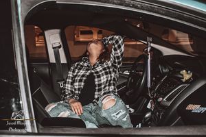 Person in plaid shirt sitting in car during indoor parking garage photoshoot.