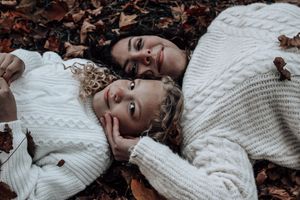 Couple in white sweaters lying among autumn leaves sharing intimate moment.