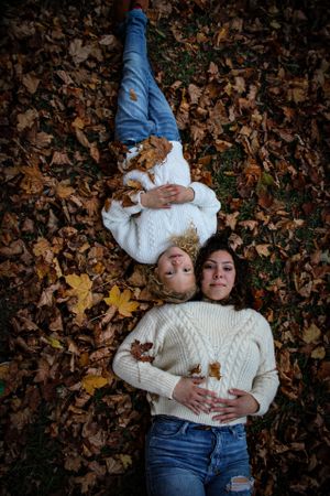 A couple in white sweaters laying on autumn leaves in a creative overhead shot.