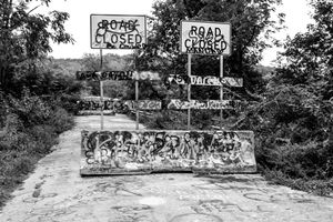 A black and white photo of graffiti-covered concrete barriers with 'Road Closed' signs.