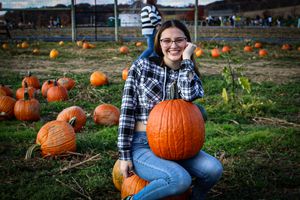 Woman smiling while holding large orange pumpkin at autumn pumpkin patch.