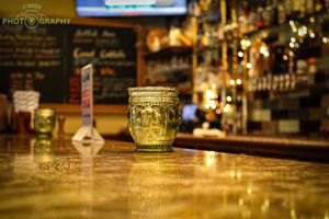 Close-up of a glass of beer on wooden bar counter with blurred pub background.