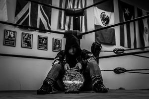 Black and white photo of someone sitting in a boxing ring with championship belt.